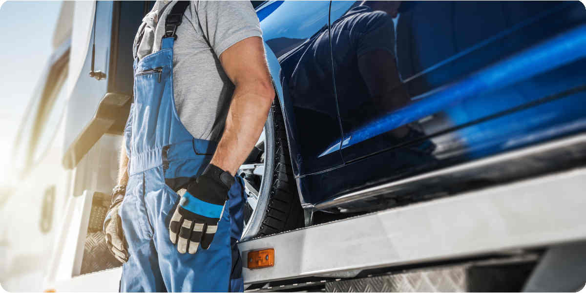 Ein Mann steht vor einem Abschleppwagen mit einem Elektroauto auf der Ladefläche.