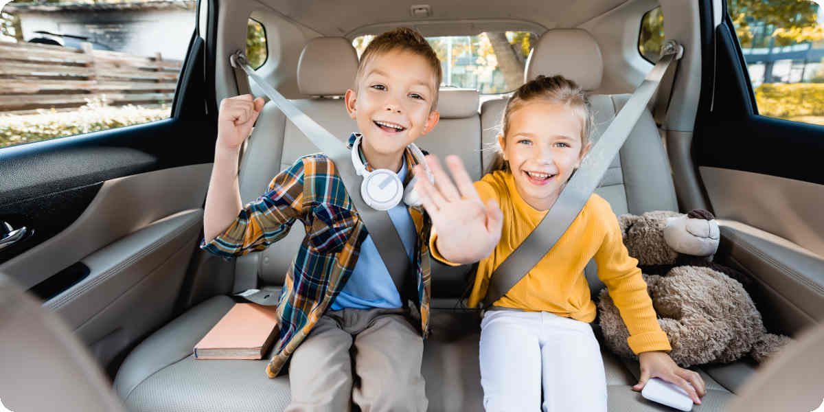 Zwei Kinder sitzen lachend auf der Rückbank eines Autos.