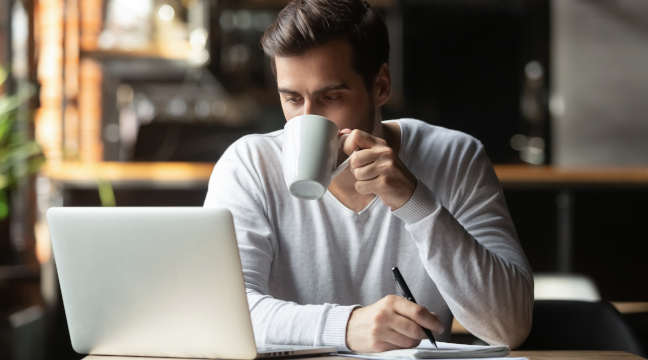 Ein Mann sitzt in einem Cafe am Laptop und liest einen Magazin Artikel.